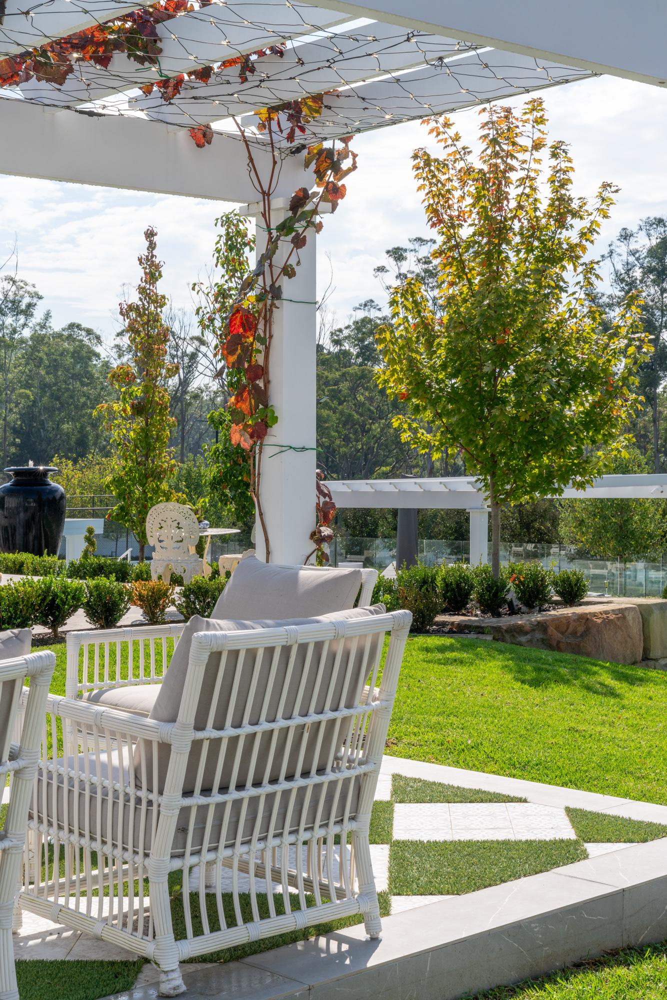 Patio with white wicker chairs, chequered stone and grass paving under a pergola