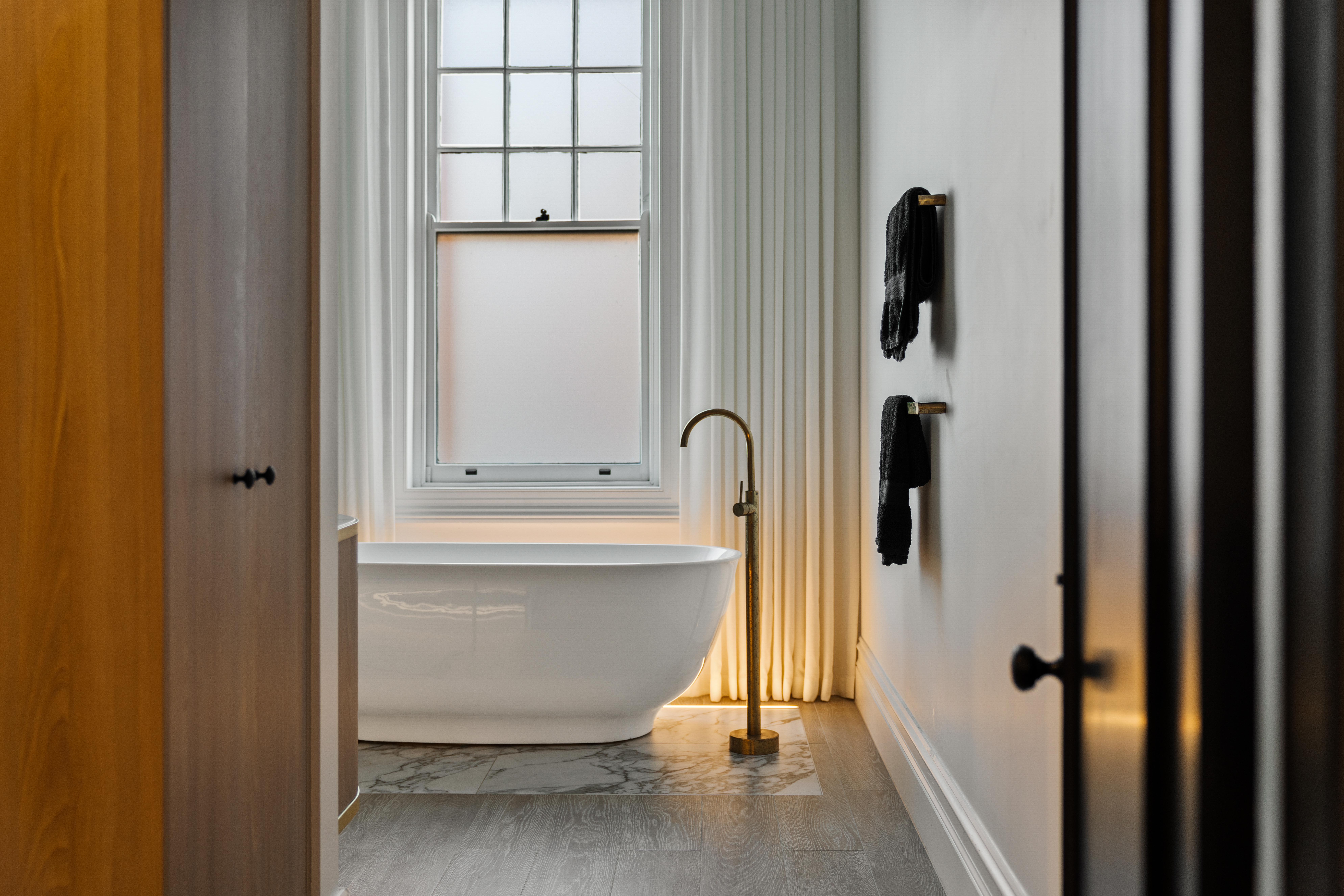 Freestanding bathtub on marble inlay with brass floor tap and sheer curtains