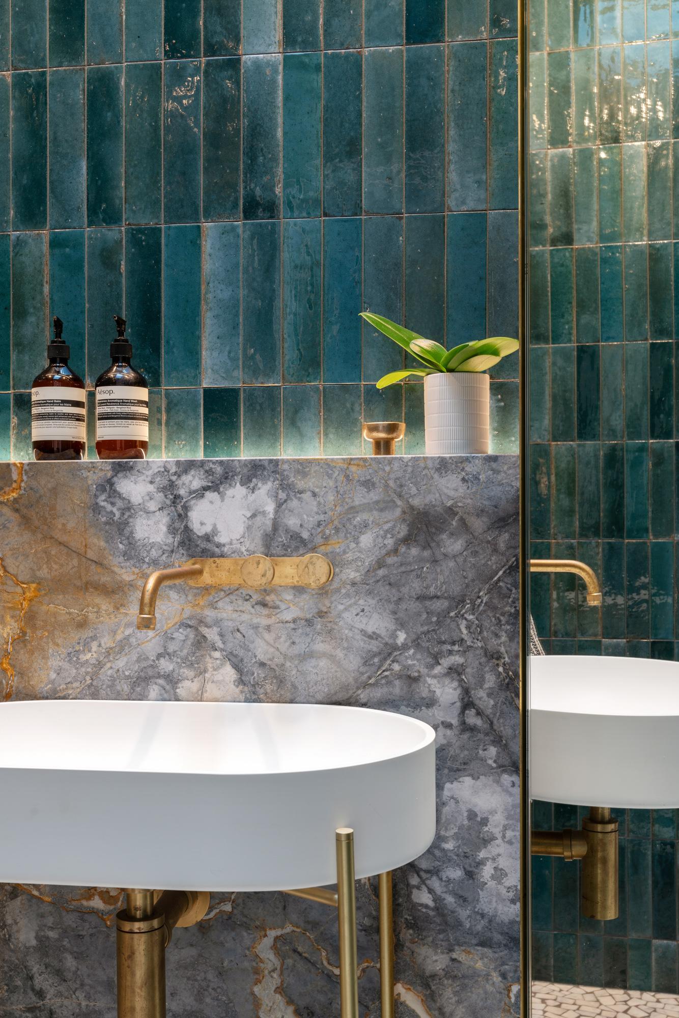 Oval vessel sink against green wall tiles and grey marble with gold fittings