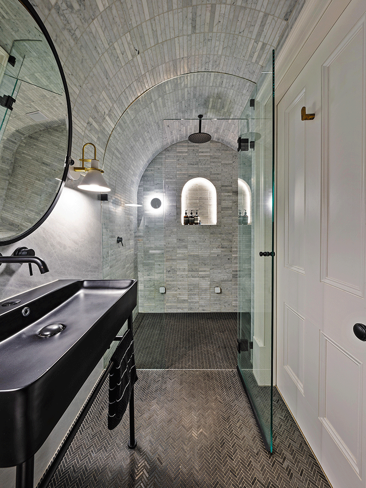 Bathroom with vaulted marble ceiling, black trough sink and glass shower