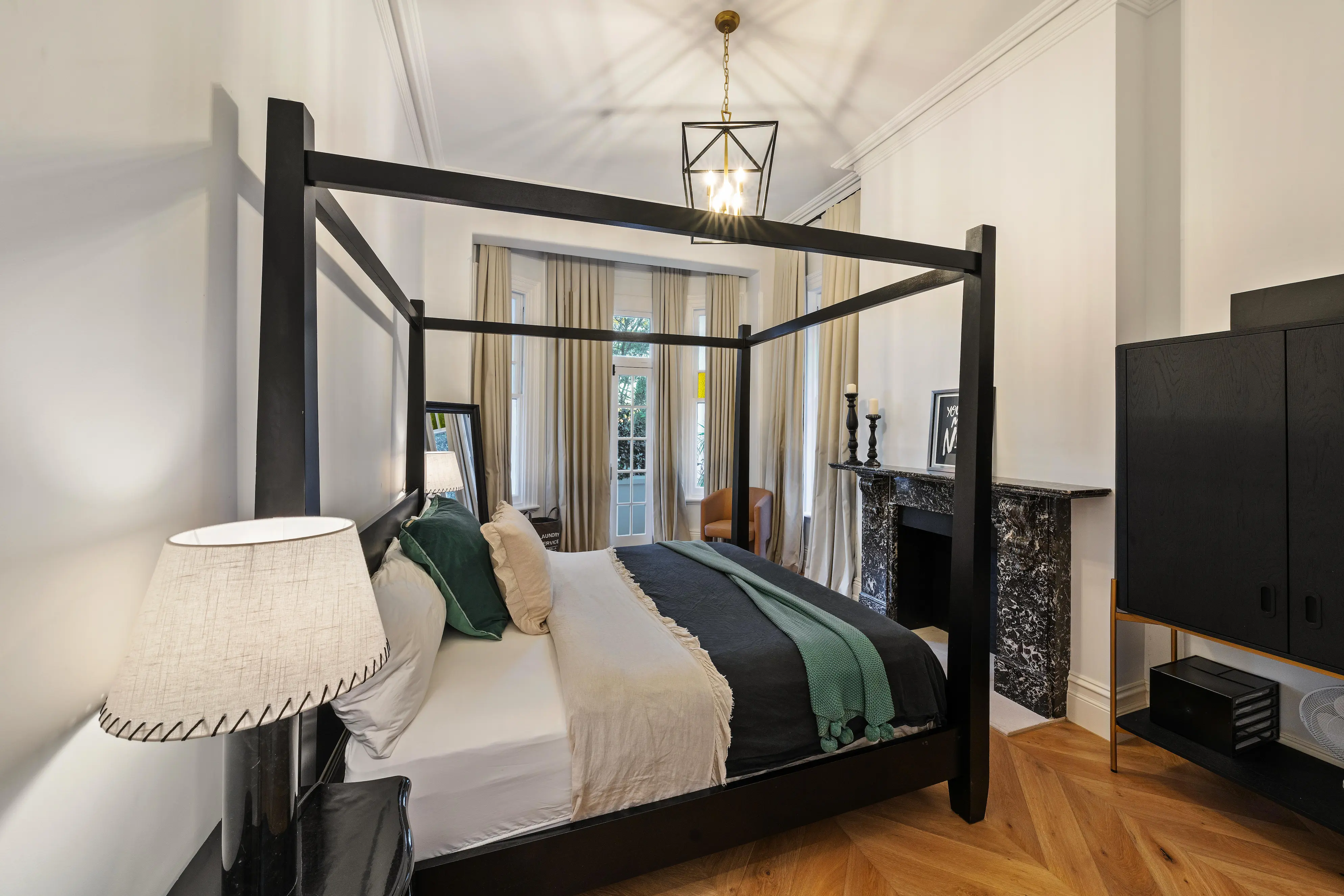 Bedroom with black four-poster bed, herringbone floors and marble fireplace