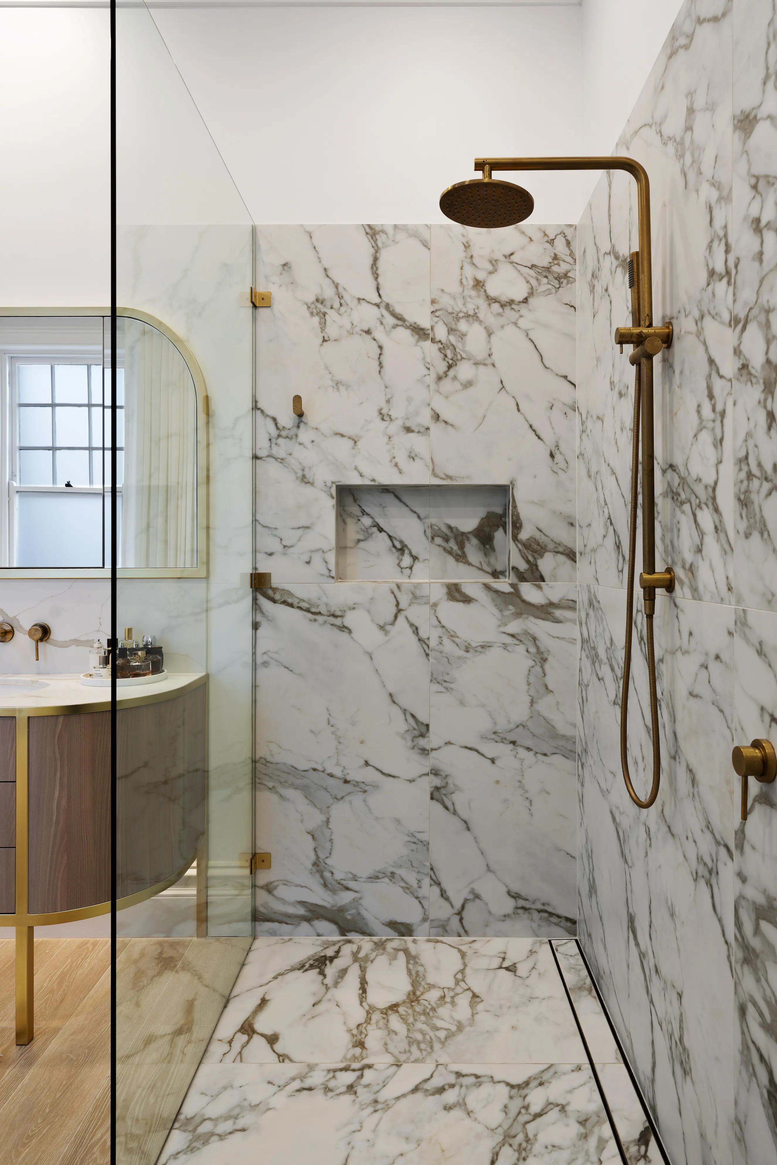Marble walk-in shower with brass fittings and frameless glass partition