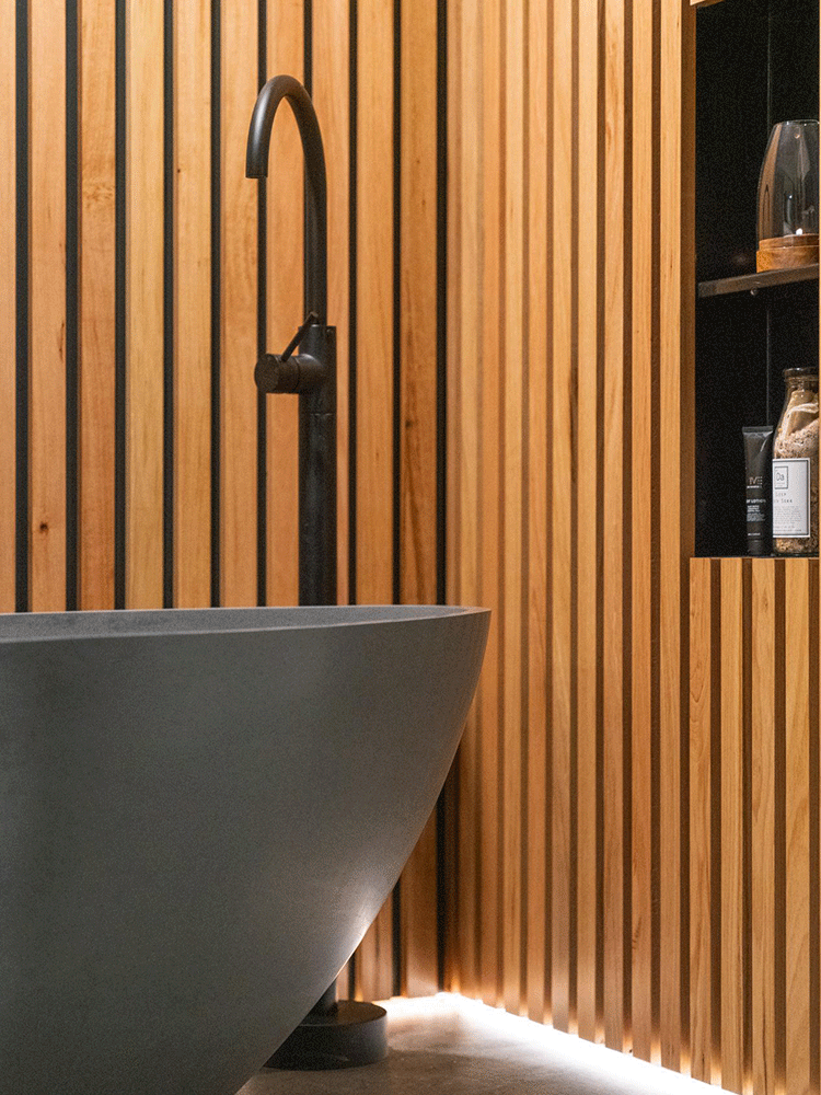 Bathroom corner with freestanding tub, timber slat wall and floor lighting