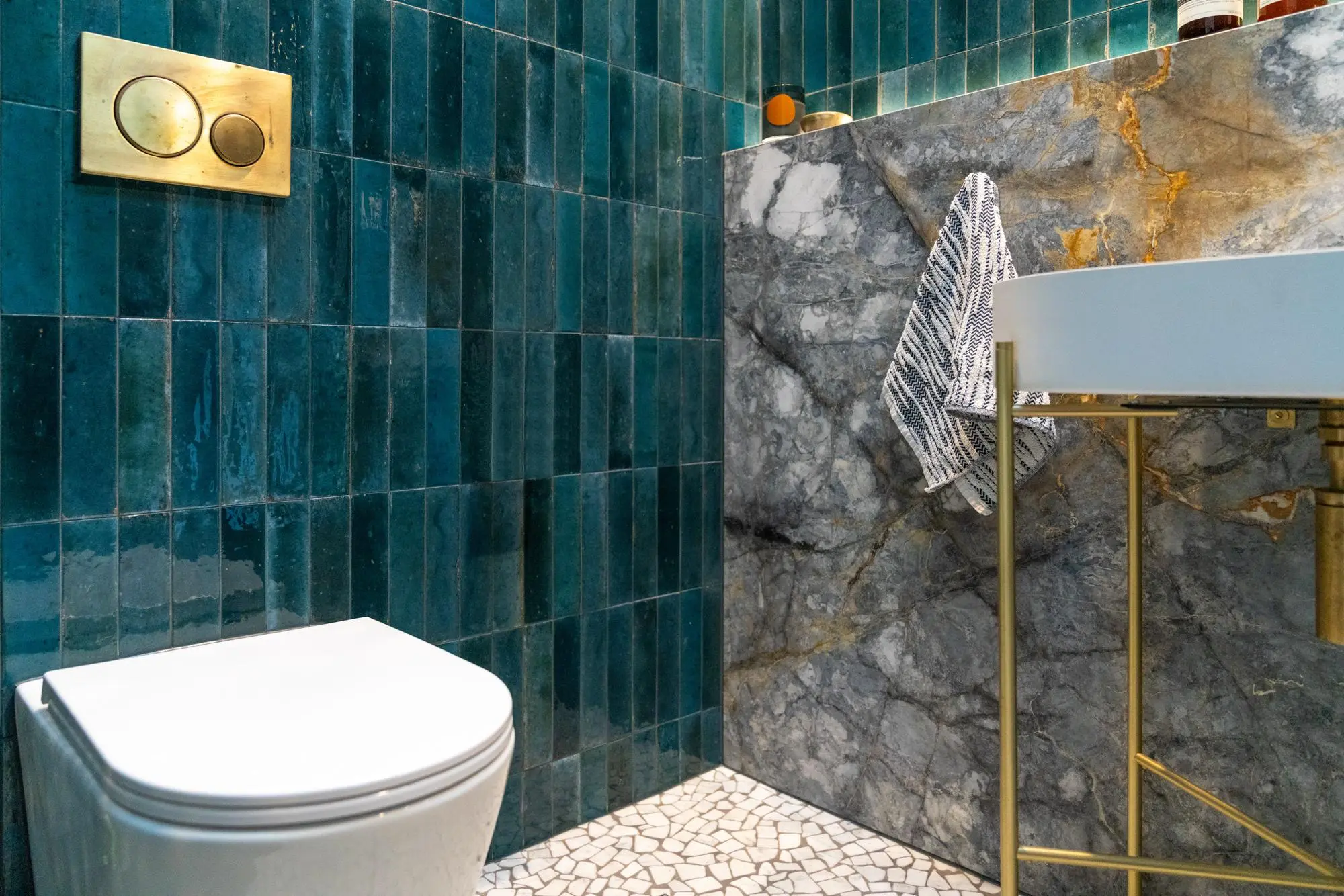 Bathroom detail with teal tiles, marble slab and brass vessel sink stand