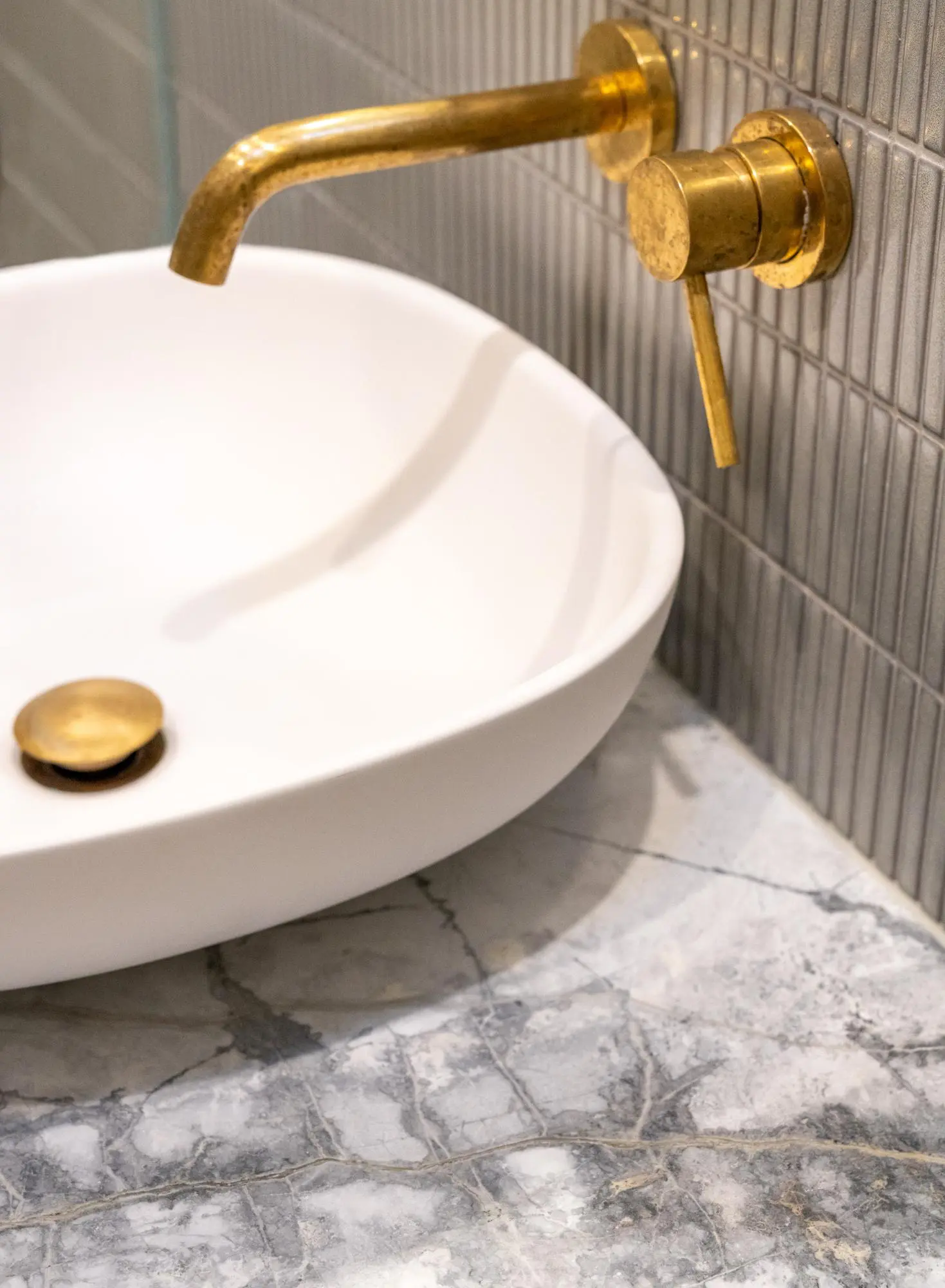 White vessel sink on marble with wall-mounted brass fittings