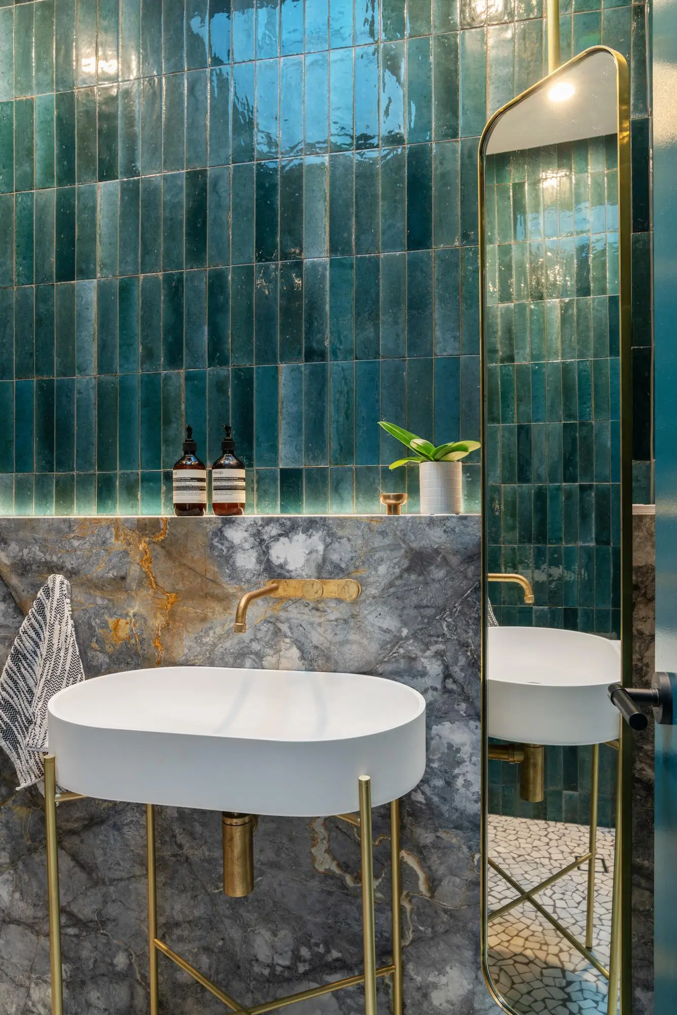 Vessel sink on brass stand against teal tiles and marble, with arched mirror